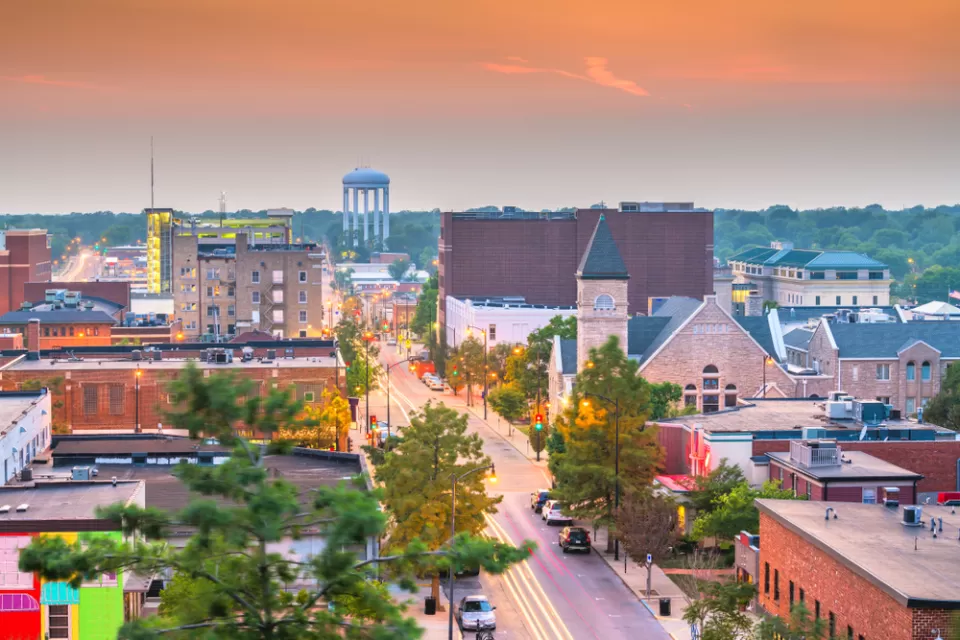A small town in the U.S. Midwest at dusk, with cars parked on a street lined with historic buildings and a water tower in the distance.